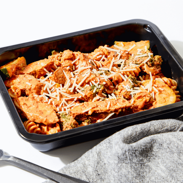 The Cajun Chicken Pasta in a meal prep container with napkin, fork and glass of water.
