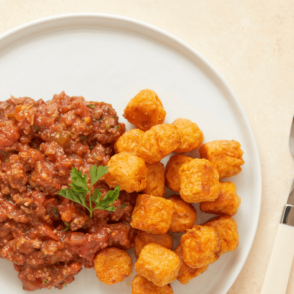 A close-up of low carb lean ground beef made with fresh tomato sauce and honey served with a side of savory sweet potato tots.