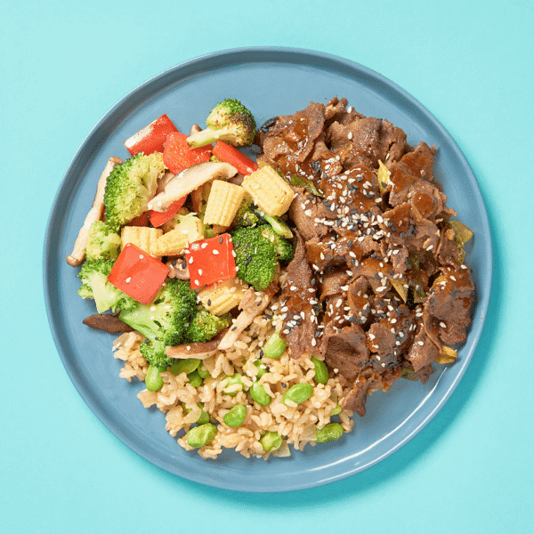 A healthy meal with Freshly Prepared Wok-seared BBQ beef, veggies, brown rice, and edamame creates a low-carb, nutritious dinner.