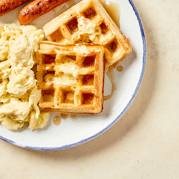 A plate of Fitlife food's FitWaffles topped with butter and maple syrup served with scrambled eggs and two chicken apple sausage links.