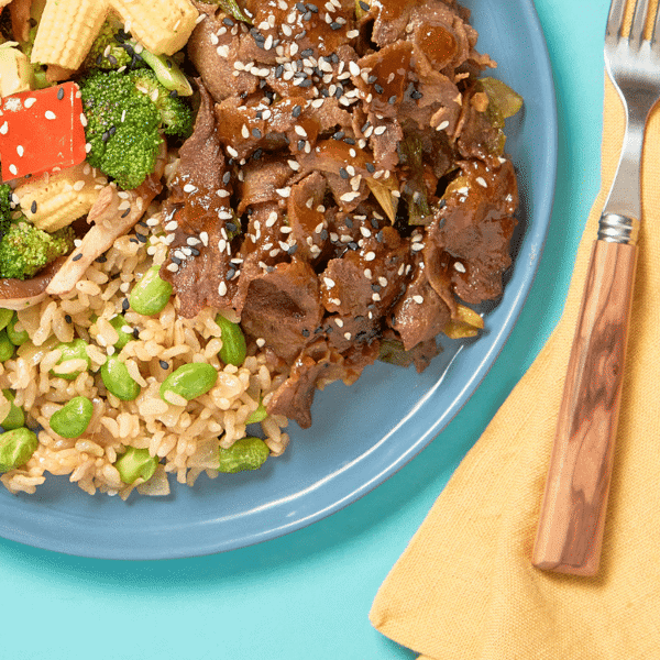A close-up of healthy, dairy-free wok-seared BBQ beef, stir-fried veggies, ginger-sesame brown rice, and edamame from Fitlife Foods.