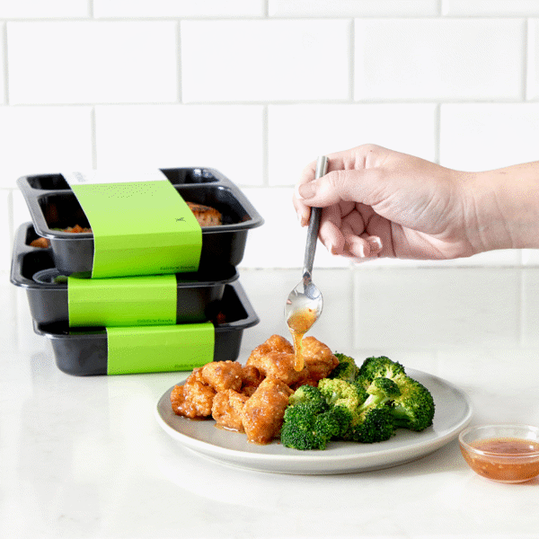 Popcorn chicken, broccoli, and orange-ginger sauce sweetened with honey as a meal prep in a food-safe box with a few boxes in the back