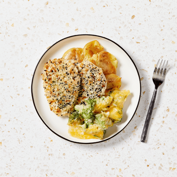 The freshly made meal of pan-seared chicken breast with herbed crust, accompanied by smashed baby potatoes and cheesy broccoli au gratin