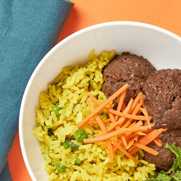 A close-up of freshly prepared lemongrass "meatballs" over turmeric rice, complemented by pickled carrots and vegan sriracha mayo.