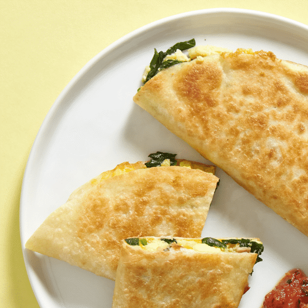 Close-up of 3 fresh breakfast quesadillas with eggs, chicken bacon, spinach, cheddar cheese, and a little bit of salsa on the side