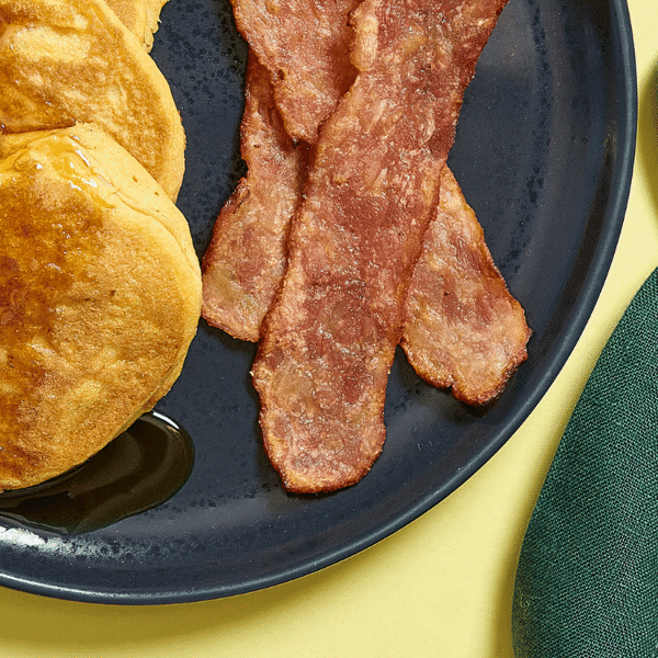 Featuring a close-up of Fitlife Foods' gluten-free pancakes paired with low-sodium chicken bacon and a side of maple syrup.