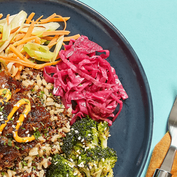 Close-up of pork, brown rice & quinoa, carrots & green onions, broccoli, sweet pickled red cabbage, and a side of spicy sesame gochu sauce.