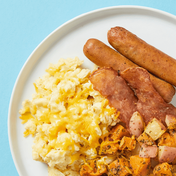 Close-up of gluten-free and low-carb breakfast meal on a plate featuring scrambled egg, sausage, bacon, and melted cheese.
