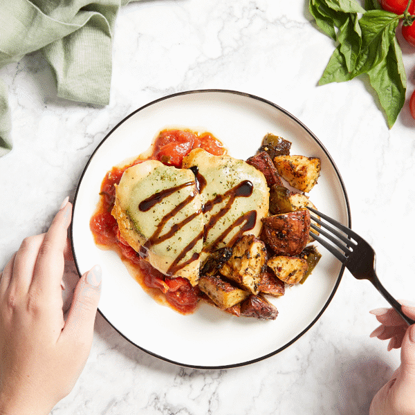 Carb-smart Chicken Caprese consists of chicken, basil pesto, provolone, balsamic drizzle, and basil pomodoro with freshly roasted veggies