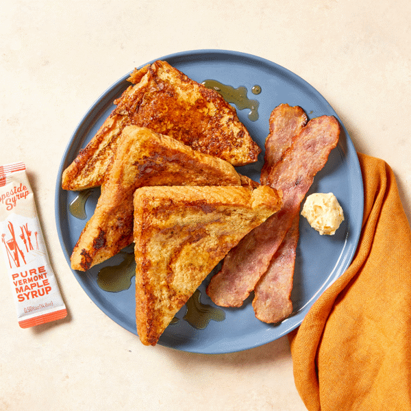 Two chicken bacon strips served with three fluffy pumpkin French toasts drizzled with plant-based butter and maple syrup.