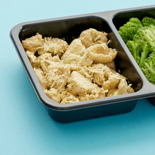 A close-up of freshly prepared whole wheat cheese tortellini, chicken, and creamy pesto-alfredo in a microwavable container